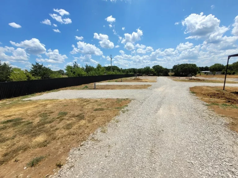 Gravel RV sites along a black privacy fence under a blue sky in Lone Grove, Oklahoma